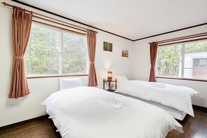 A hotel room with two beds, a nightstand, a lamp, and large windows with curtains. - Chalet Strickland (Hakuba)