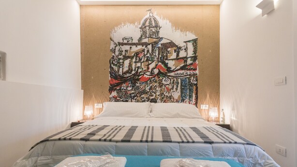 A hotel room with a large bed, a blue accent wall, and a mural depicting a cityscape. - Ballarò Suite Behind the Cathedral (Palermo)