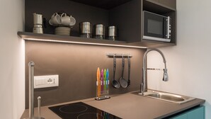 A modern kitchen with a built-in induction cooktop, a stainless steel sink, and a microwave above the counter. - Ballarò Suite Behind the Cathedral (Palermo)