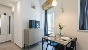 A modern kitchen with a dining area, a TV on a cabinet, and a window with curtains. - Ballarò Suite Behind the Cathedral (Palermo)