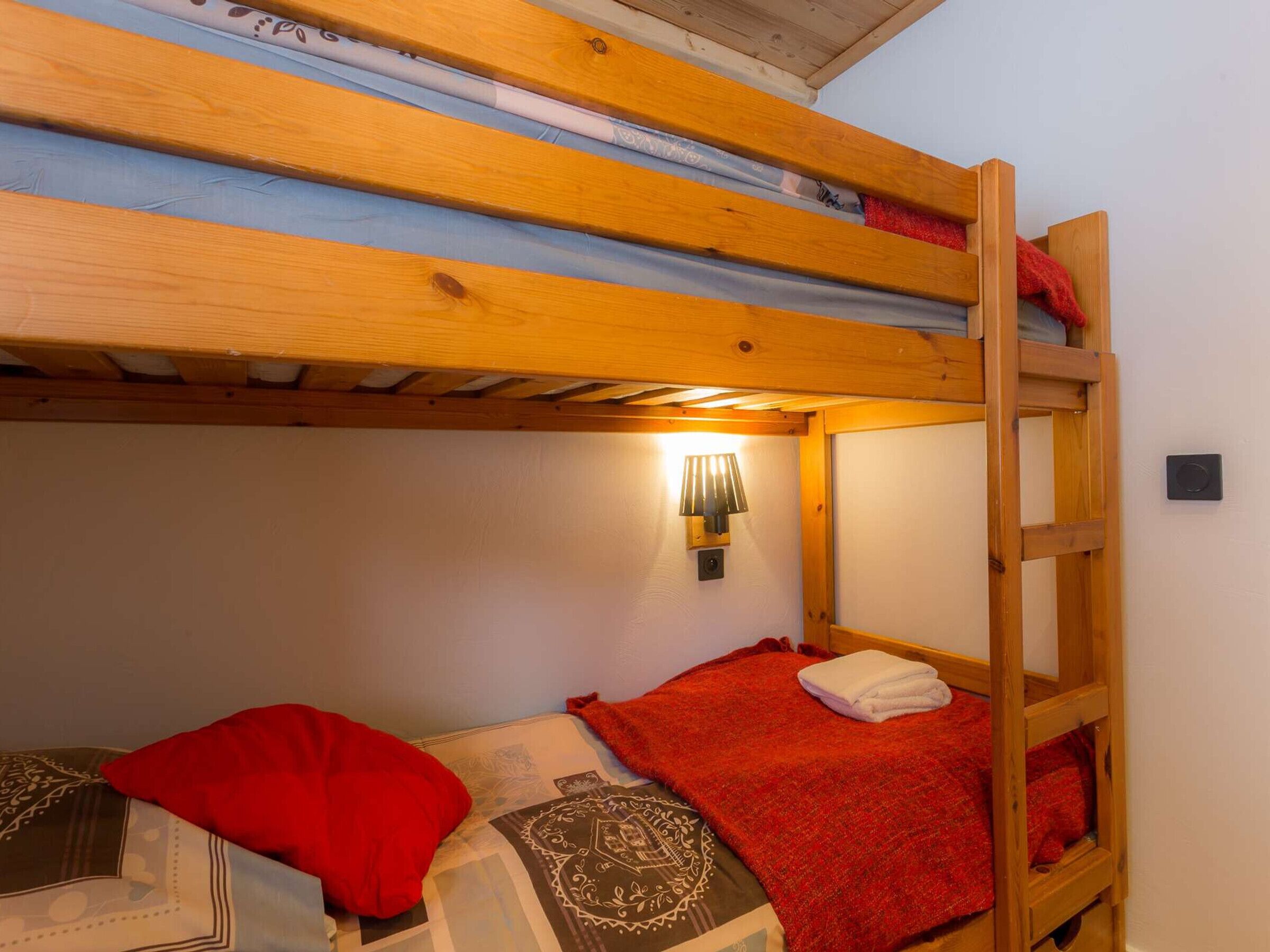 Ein Schlafraum mit Etagenbetten, Holzboden, einer Wandleuchte und einer roten Decke auf dem untersten Bett.