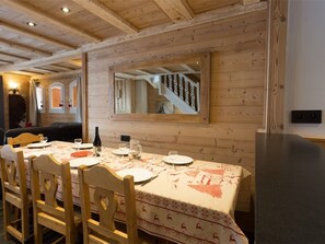 Un comedor con una mesa de madera dispuesta para cuatro, un espejo en la pared y una escalera al fondo.