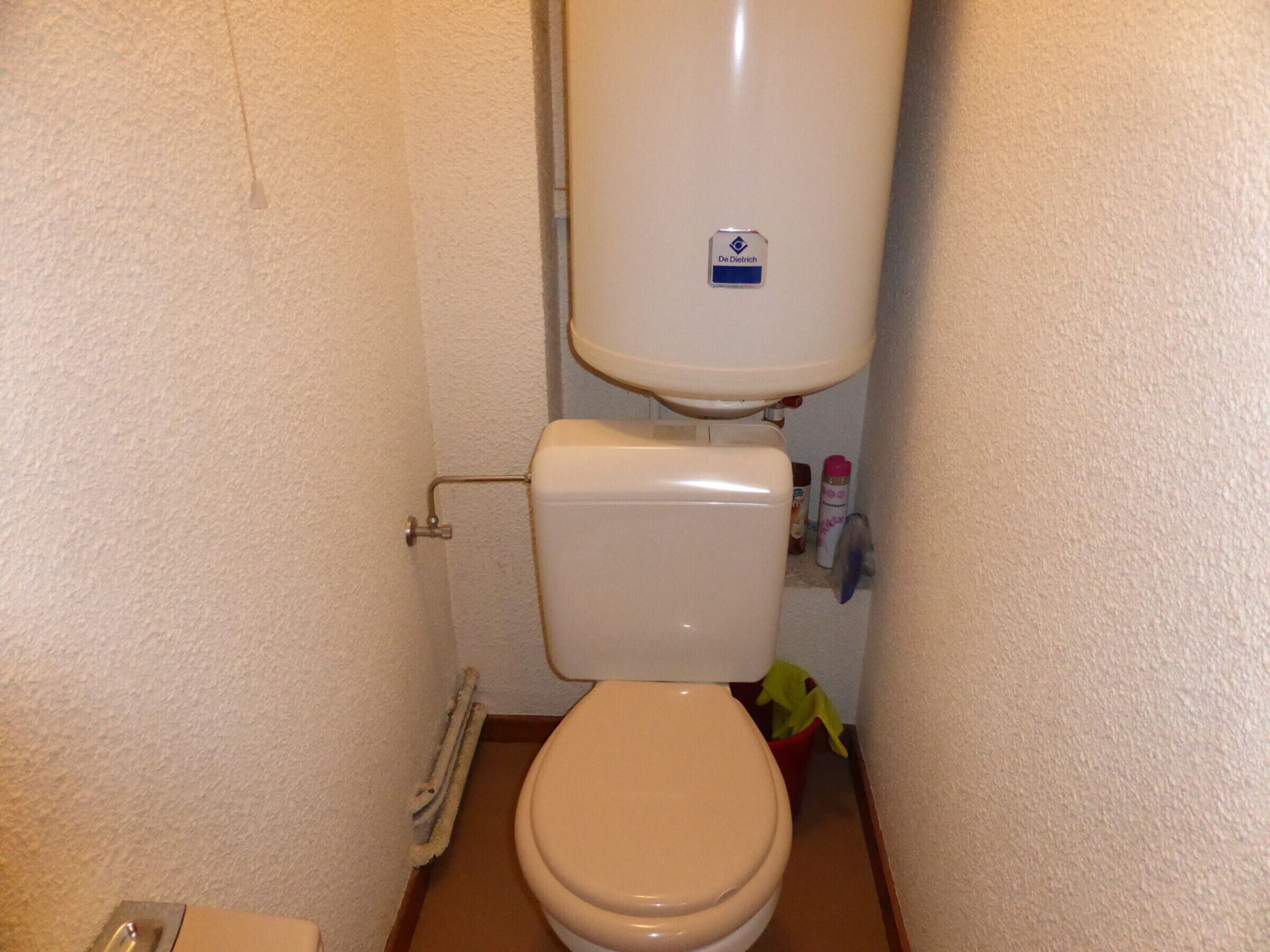 Une petite salle de bain avec des toilettes, un mur blanc et une tuyauterie apparente.