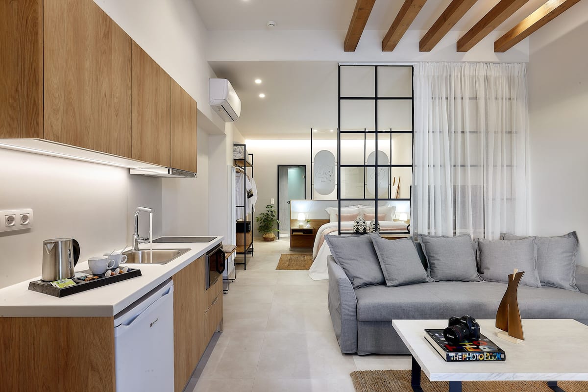 A modern kitchen with a dishwasher, a coffee maker, and a tray of muffins. There is a grey sofa and a coffee table with a book and a camera.