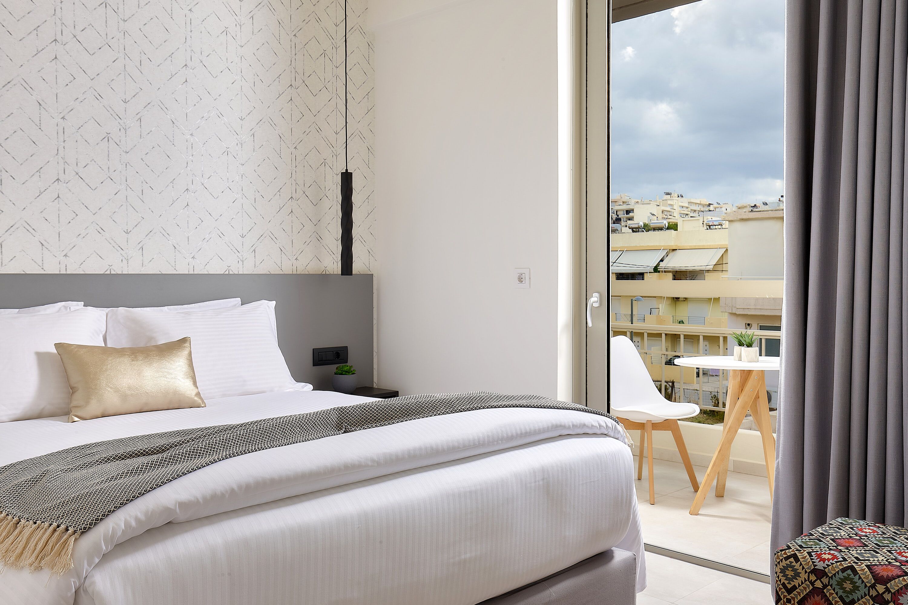 Ein modernes Hotelzimmer mit einem großen Bett, einem Nachttisch mit Lampe und Blick auf die Stadt vom Balkon aus.