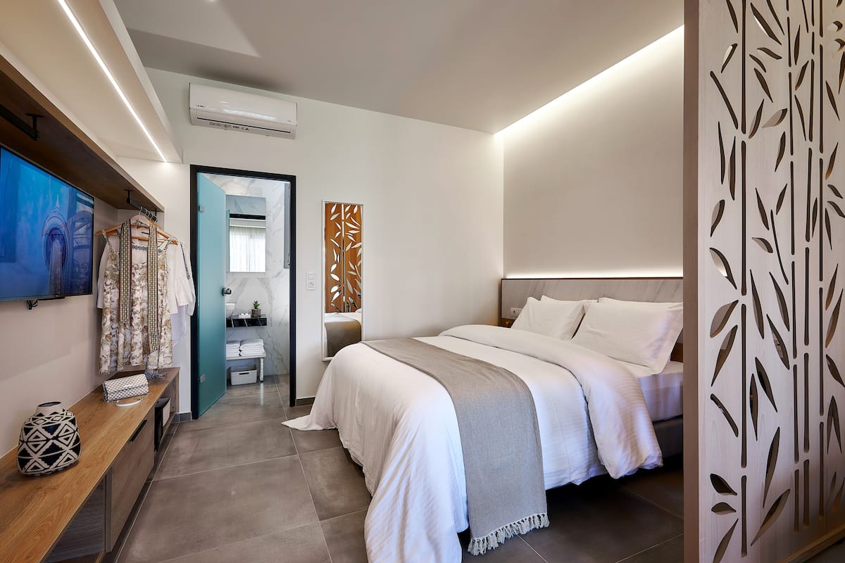 A modern hotel room with a large bed, a TV, a wooden console table, and a bathroom visible through an open door.