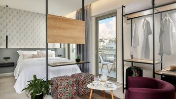 A modern hotel room with a bed, a seating area with a table, a wardrobe, and a balcony with clothes hanging.