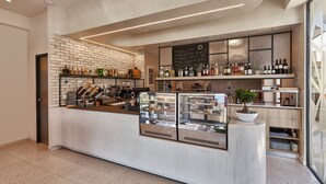 A modern coffee shop with a brick wall, a counter with various coffee machines, and shelves stocked with beverages. - Stay 365 Heraklion Apart Hotel (Heraklion)