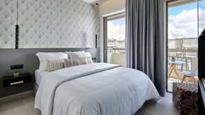 A modern bedroom with a large bed, a nightstand, a small table with a plant, and a balcony with a view of the city. - Stay 365 Heraklion Apart Hotel (Heraklion)