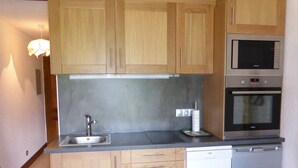 A compact kitchen with wooden cabinets, a stainless steel sink, a microwave, and an oven. - Studio for 4, opposite ski lift, private terrace (Combloux)
