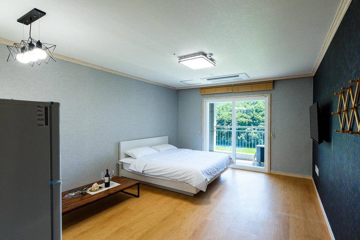 Une chambre avec un lit, une petite table sur laquelle se trouvent une bouteille et des verres, un téléviseur fixé au mur et une fenêtre donnant sur un paysage verdoyant.