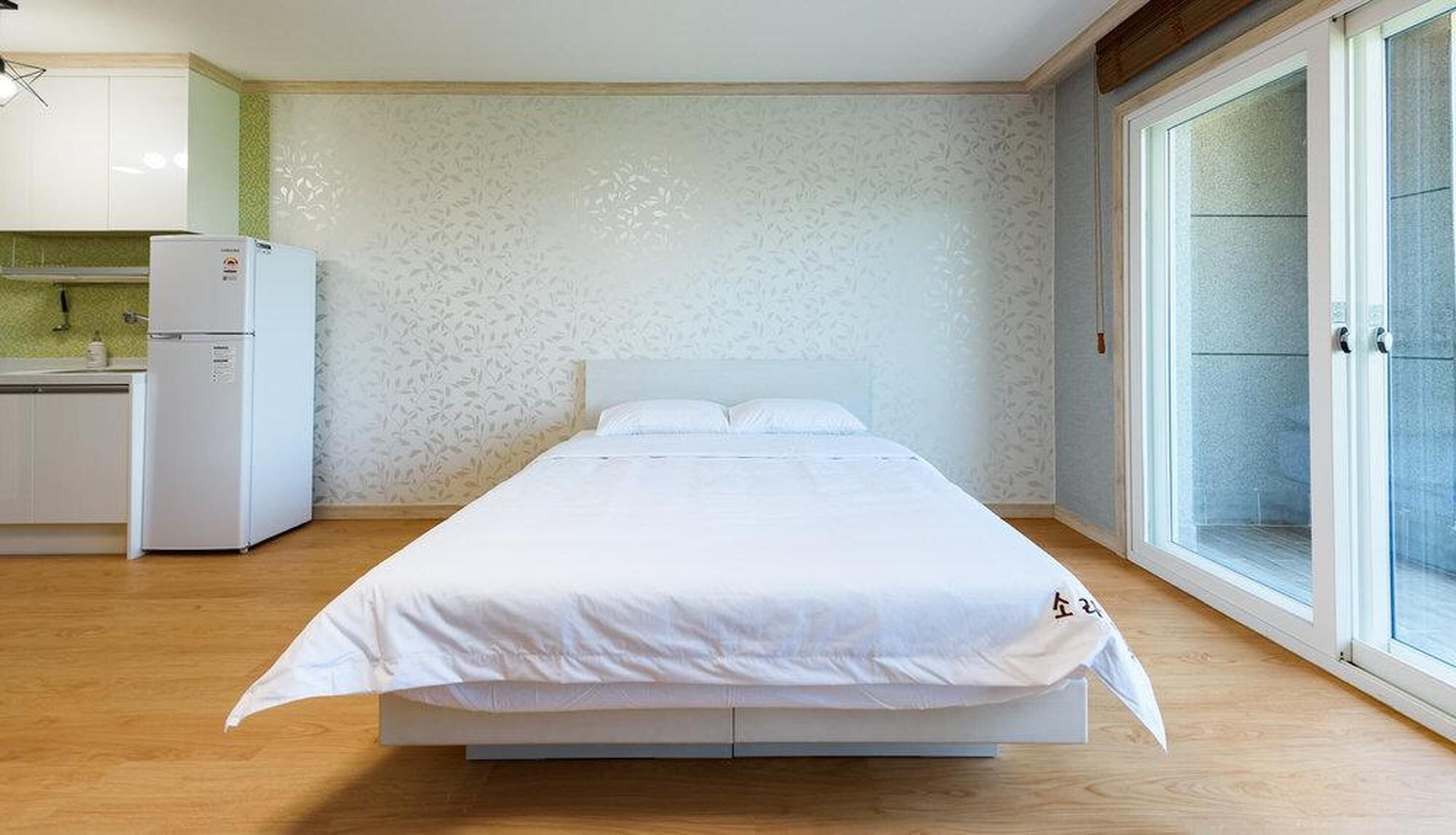 A bedroom with a bed, a small kitchenette, and a sliding glass door to a balcony.