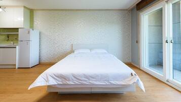 A bedroom with a bed, a small kitchenette, and a sliding glass door to a balcony.