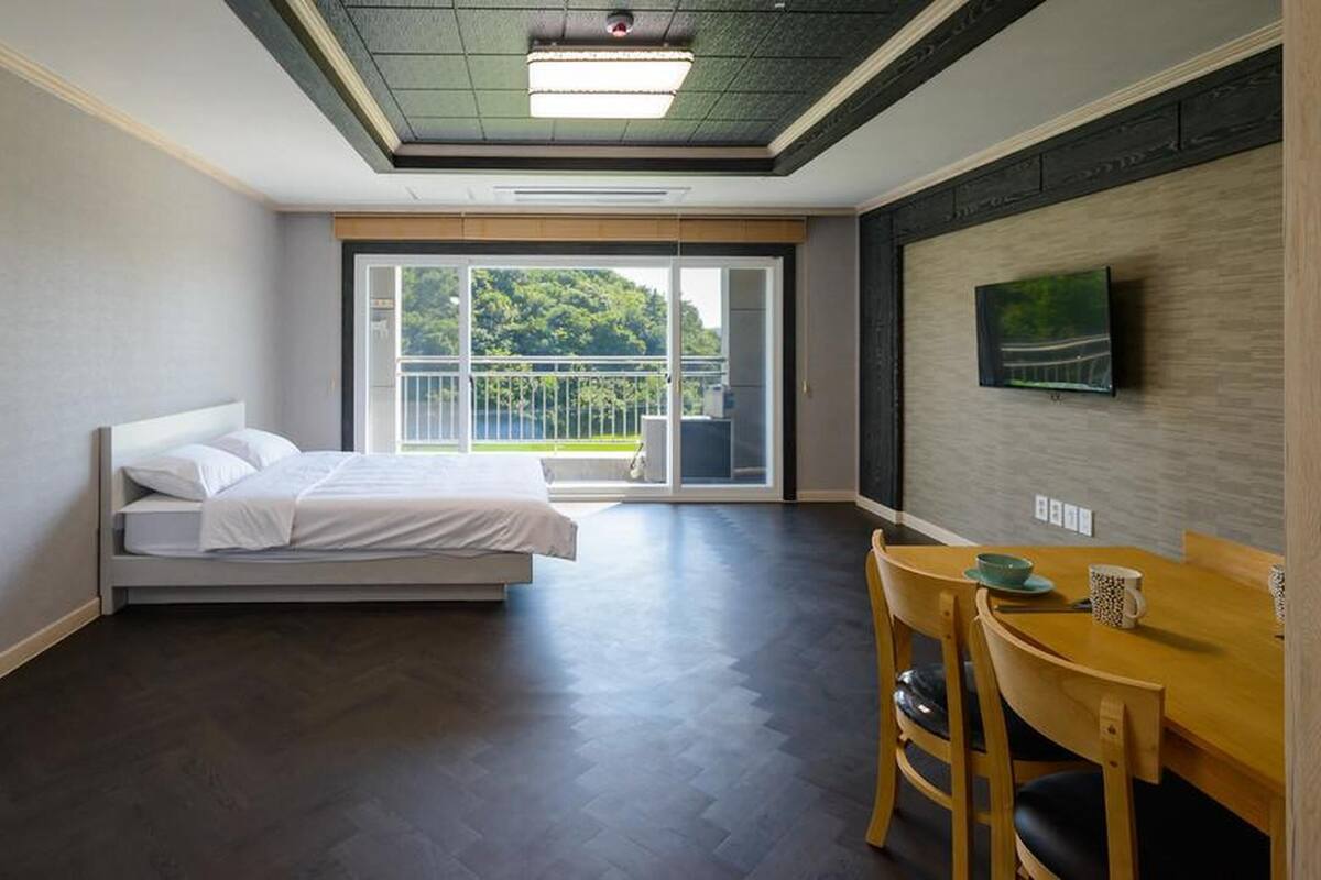 Une chambre d’hôtel comprenant un lit, une table à manger avec des chaises, un téléviseur fixé au mur et une porte-fenêtre coulissante donnant sur un espace extérieur.