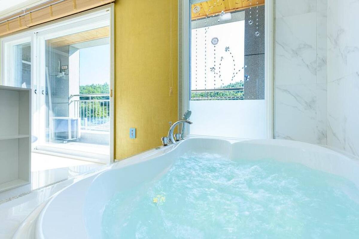 Une salle de bain dotée d’une grande baignoire, d’une porte vitrée donnant sur un balcon et offrant une vue sur la verdure environnante.