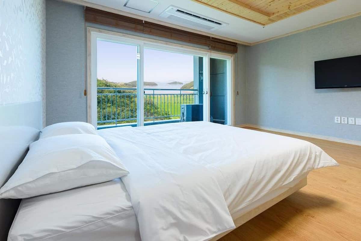 Une chambre avec un grand lit, un téléviseur fixé au mur et un balcon avec vue.