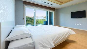 A bedroom with a large bed, a TV mounted on the wall, and a balcony with a view.