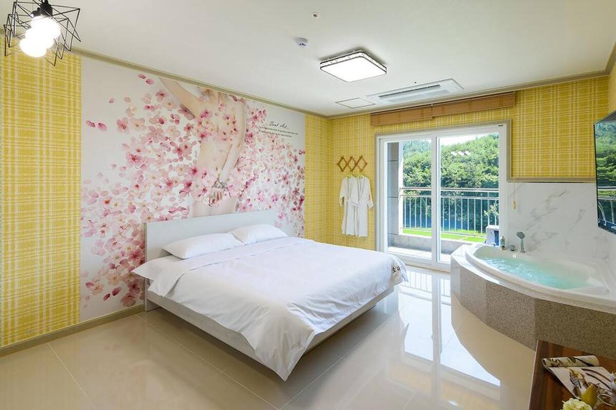 Une chambre moderne avec un grand lit, une baignoire et un balcon donnant sur un paysage verdoyant.