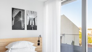 A hotel room with a wooden headboard, a bed with white linens, a nightstand with a lamp, and two black and white photographs on the wall. - LUXURIOUS, BRIGHT & LARGE TERRACE WITH GREAT VIEW | Family-Friendly (Lisboa)