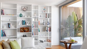 A modern living room with a white sofa, a coffee table, and a bookshelf filled with books and decorative items. - LUXURIOUS, BRIGHT & LARGE TERRACE WITH GREAT VIEW | Family-Friendly (Lisboa)