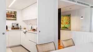 A modern kitchen with white cabinets, a dining area with a white table and two chairs, and a painting of a tree on the wall. - LUXURIOUS, BRIGHT & LARGE TERRACE WITH GREAT VIEW | Family-Friendly (Lisboa)