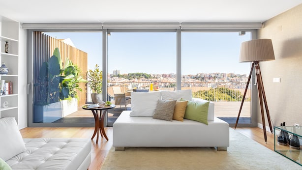 A modern living room with a white sofa, a glass coffee table, and a large window offering a city view. - LUXURIOUS, BRIGHT & LARGE TERRACE WITH GREAT VIEW | Family-Friendly (Lisboa)