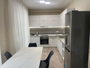A modern kitchen with white cabinets, a stainless steel refrigerator, a built-in oven, and a dining table with chairs.