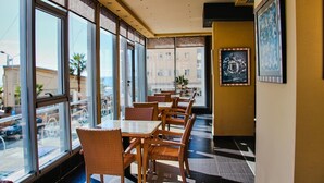 Um restaurante com grandes janelas, cadeiras de vime e mesas.