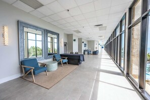 A spacious hallway with large windows, a seating area with blue chairs, and a reception desk.