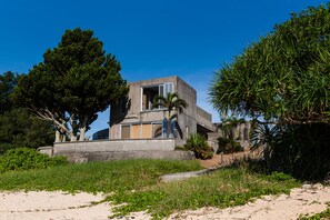 A modern concrete building with a large open window and a door, surrounded by lush greenery and trees.