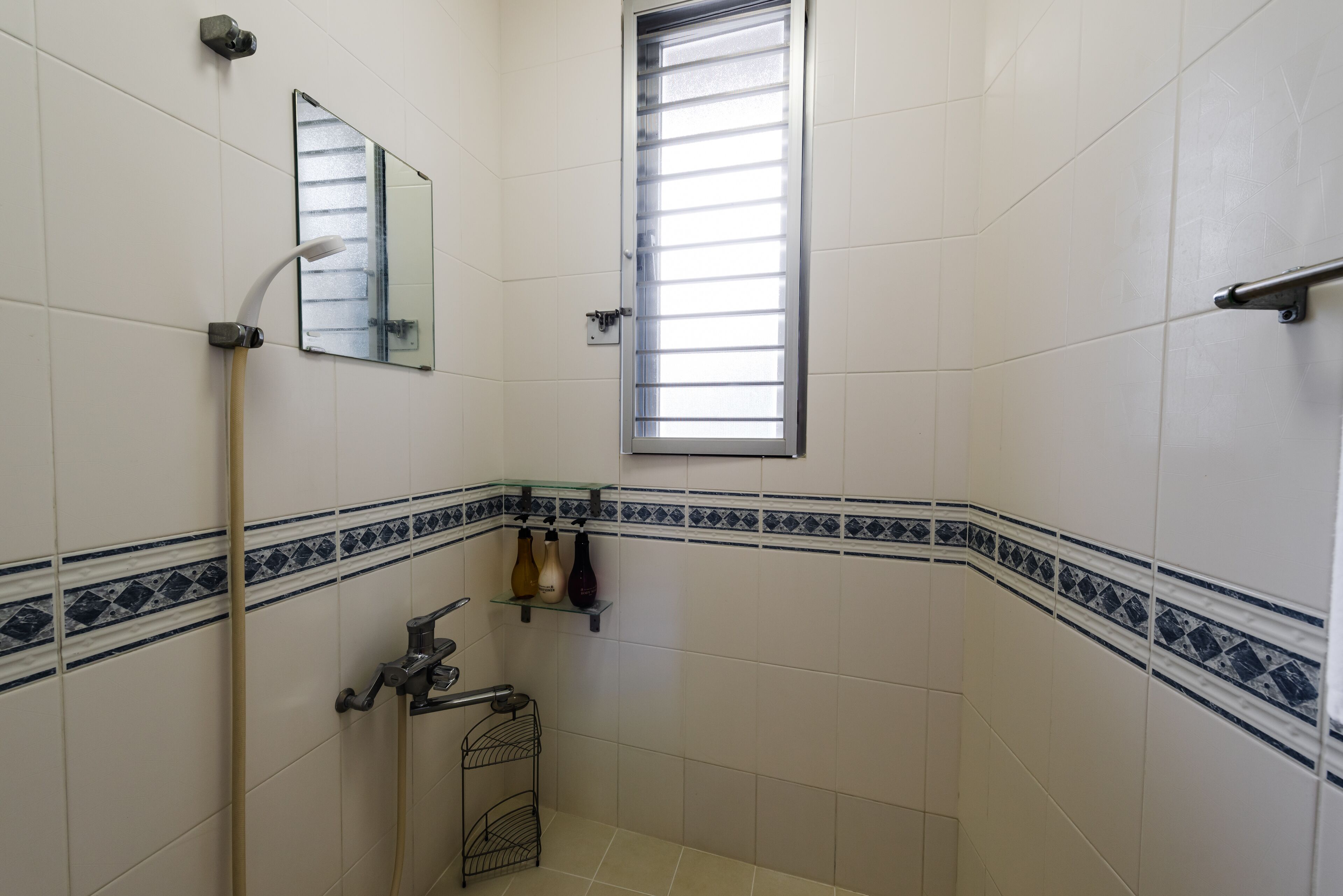 A bathroom with white tiles, a window, a mirror, a shower, and a towel rack.