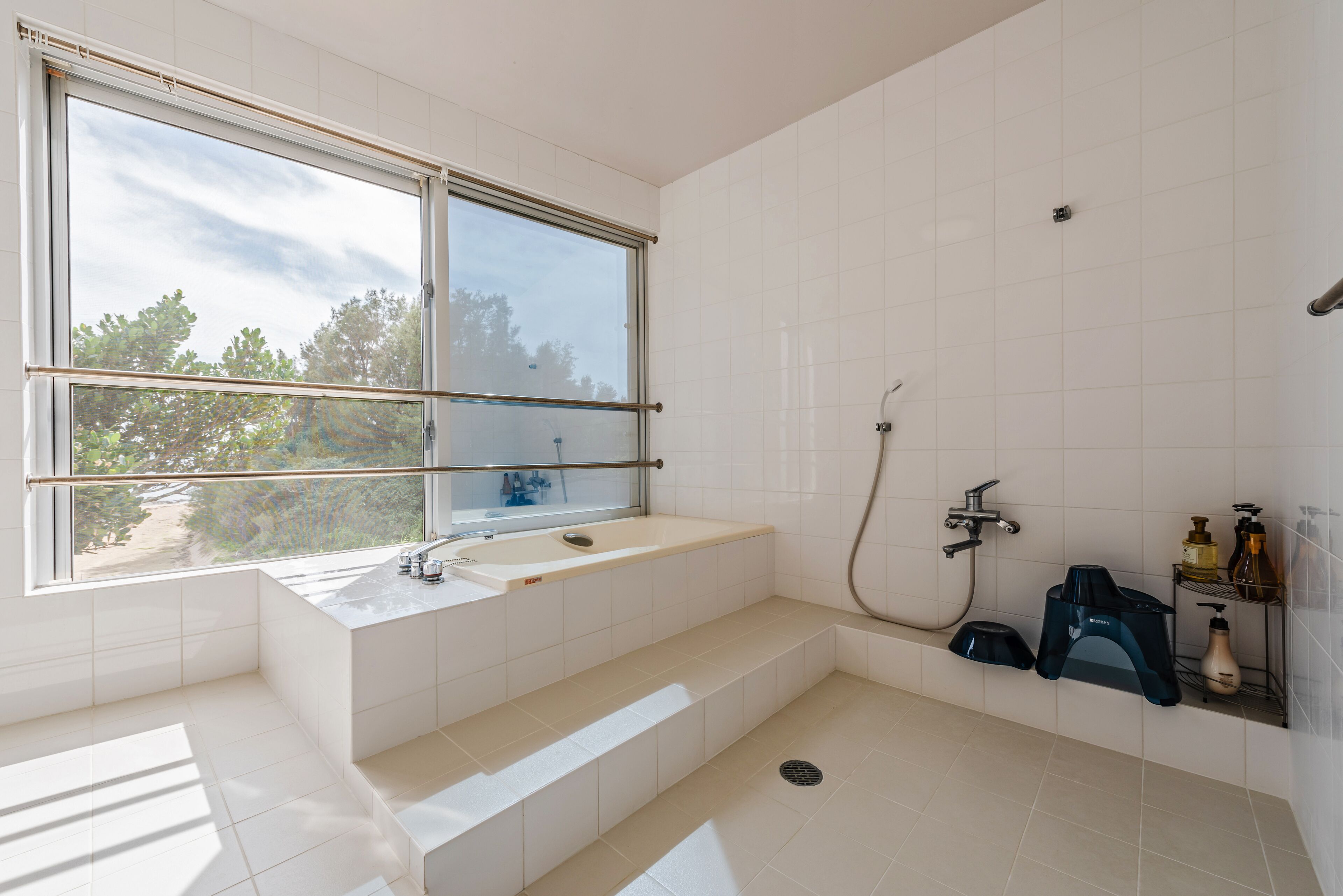 A modern bathroom with a large window, a bathtub, a shower, and a toilet.