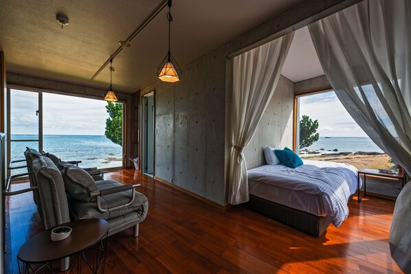 A bedroom with a large bed, a sofa, and a view of the beach.