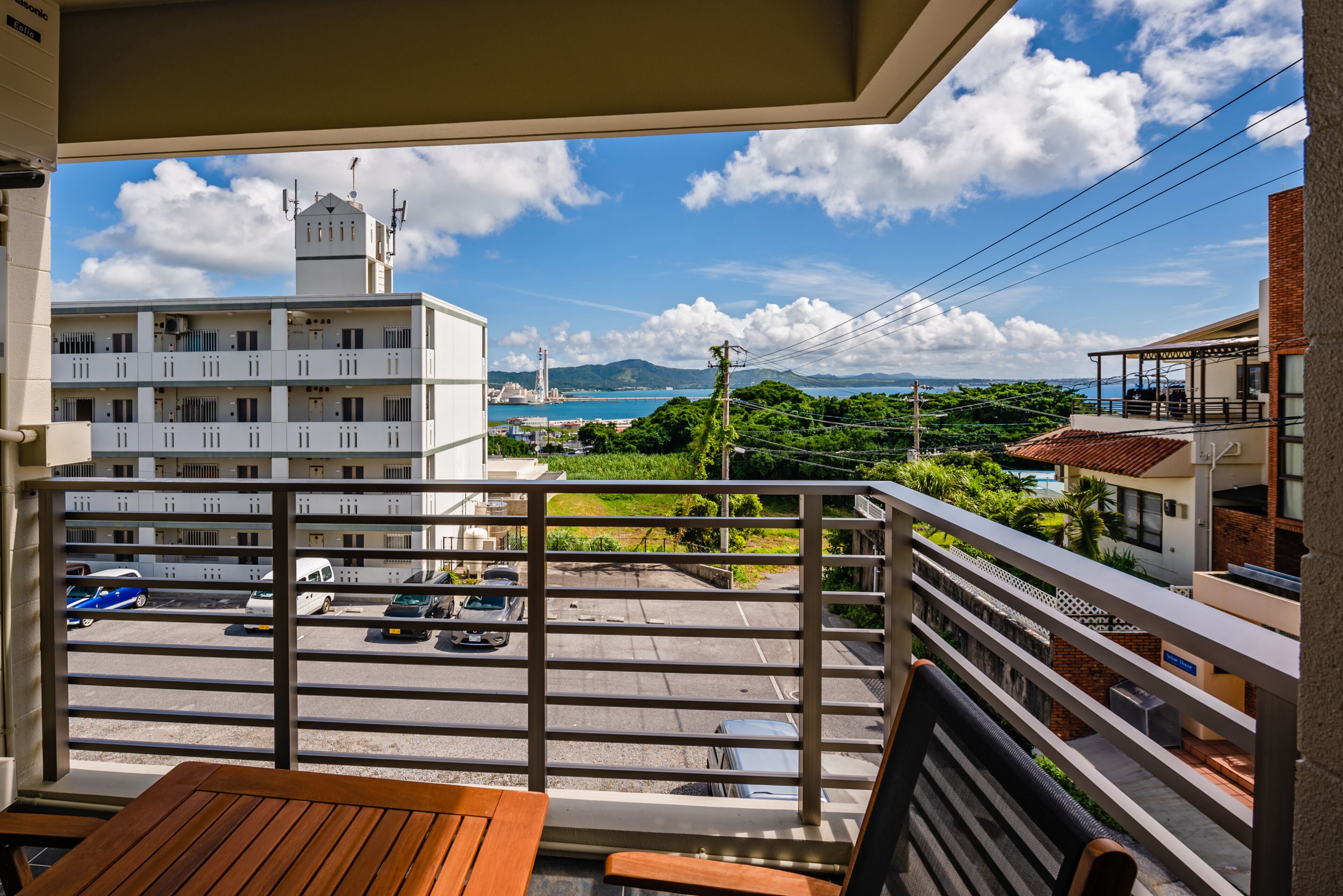 A balcony with a view of a parking lot, buildings, and a distant coastline.