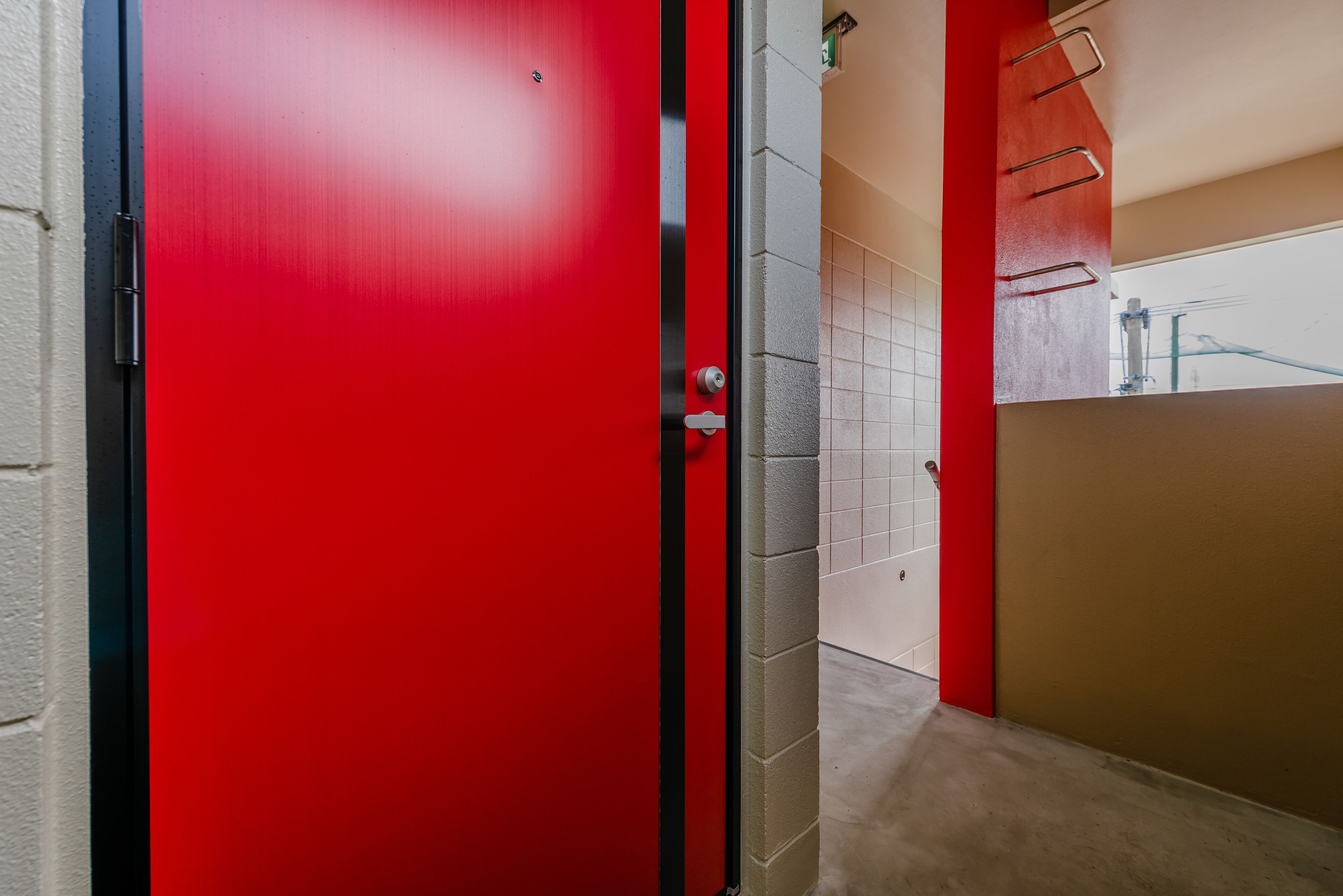 A red door with a metal handle, a tiled wall, and a beige floor.
