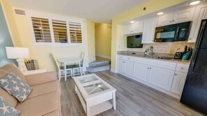 A compact living space with a kitchenette, a dining area with a white table and chairs, and a sofa with patterned cushions.