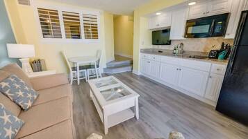 A compact living space with a kitchenette, a dining area with a white table and chairs, and a sofa with patterned cushions.