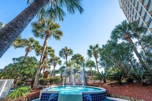 Una piscina con una fuente rodeada de palmeras y un edificio al fondo.