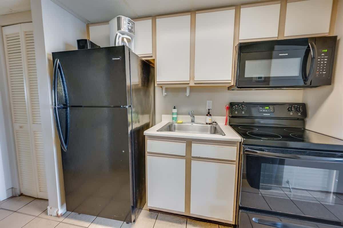 Een kleine keuken met een koelkast, magnetron, fornuis en spoelbak.
