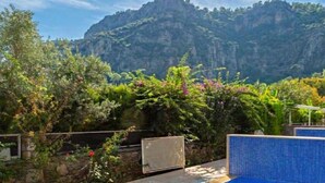 Una piscina con borde de azulejos, rodeada de exuberante vegetación y un telón de fondo montañoso.