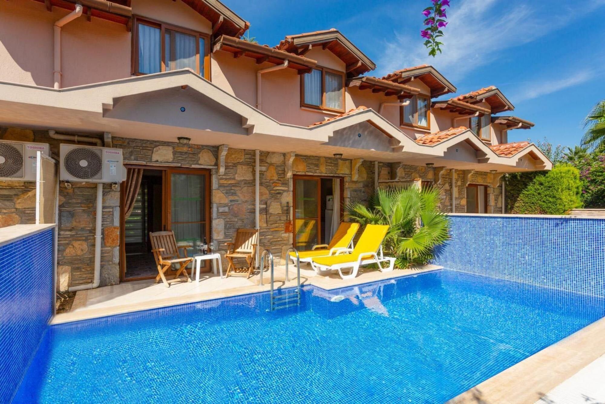 Una casa de dos pisos con fachada de piedra, piscina y mobiliario de exterior.