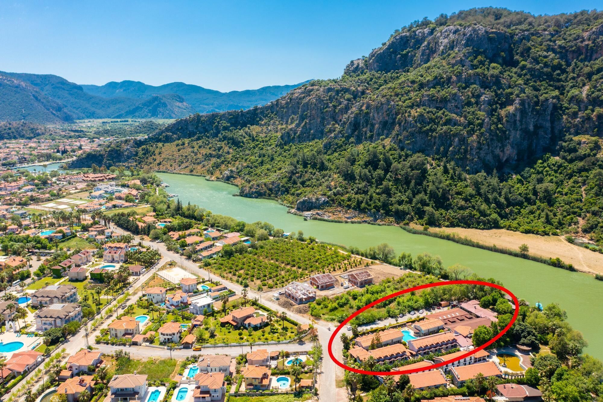 Une ville côtière traversée par une rivière, entourée de collines. Un cercle rouge met en évidence un bâtiment doté d’une piscine.