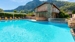 A swimming pool with a bar area, surrounded by lounge chairs, set against a mountainous backdrop. - Villa Elmas Paradise (Ortaca)