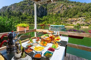 A table set with food and drinks, a cactus, and a teapot on a deck overlooking a lake with a boat and greenery in the background. - Villa Ayla Paradise in Dalyan (Ortaca)