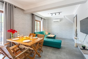 Una sala de estar moderna con una mesa de comedor de madera, un sofá color turquesa y un televisor de pantalla plana montado en la pared.