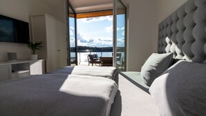 A modern bedroom with a large bed, a TV, and a view of a lake through a glass door. - Exclusive and modern holiday home "Lilla älg" right on the lake 365 days a year! (Arvika)