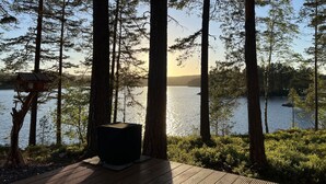 Eine Holzterrasse mit Blick auf einen See, umgeben von hohen Bäumen und einem Vogelhäuschen.