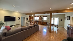 A spacious living room with a large sectional sofa, wooden flooring, and a flat-screen TV mounted on the wall. - Country Quiet 3 Bedroom 2 Bath Tranquil Space! (Millsboro)