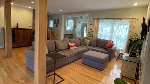 A spacious living area with a large sectional sofa, wooden flooring, and a view of the kitchen through an open doorway. - Country Quiet 3 Bedroom 2 Bath Tranquil Space! (Millsboro)