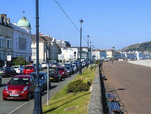Calle con coches estacionados y edificios, una banca y cielo despejado.